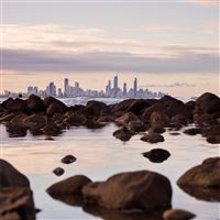 seashore rocks near city view of buildings 5k wallpaper