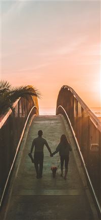 man and woman holding hand while walking on bridge iPhone 11 wallpaper