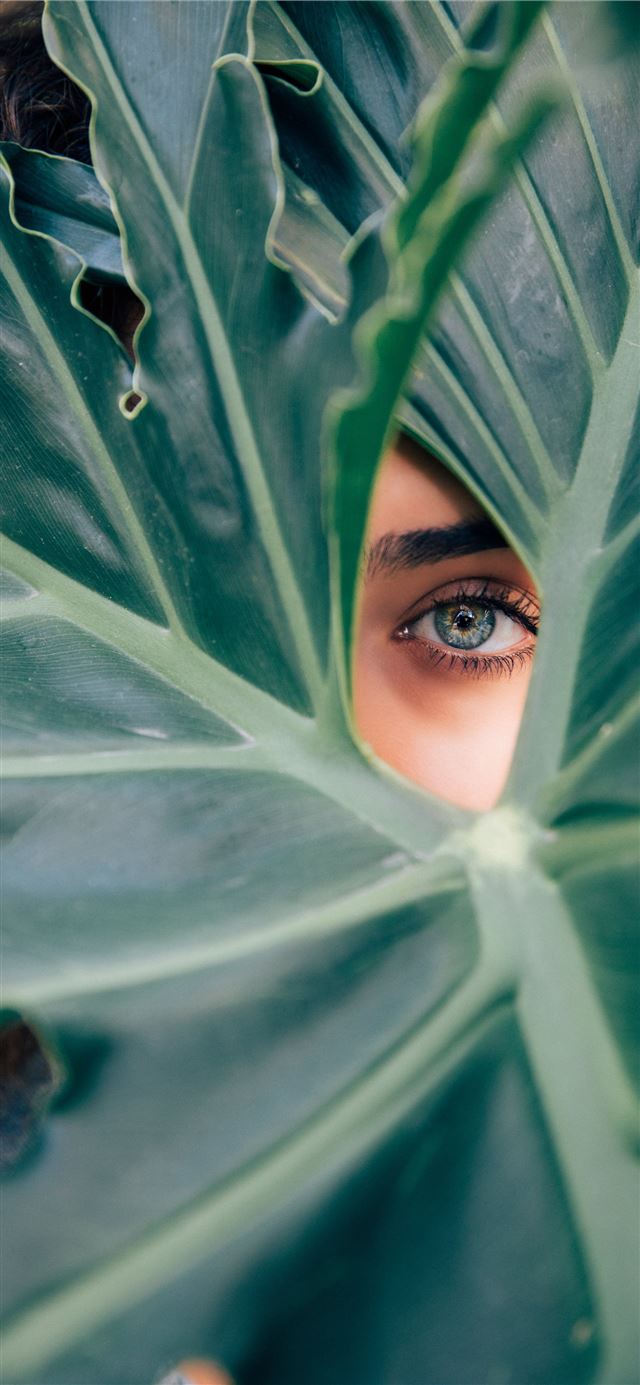 1125x2436 woman peeking over green leaf plant taken at dayti... - beauty iPhone 11 Wallpaper