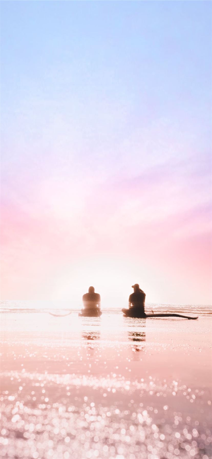 silhouette of two person sitting on seashore durin... iPhone 11 wallpaper 