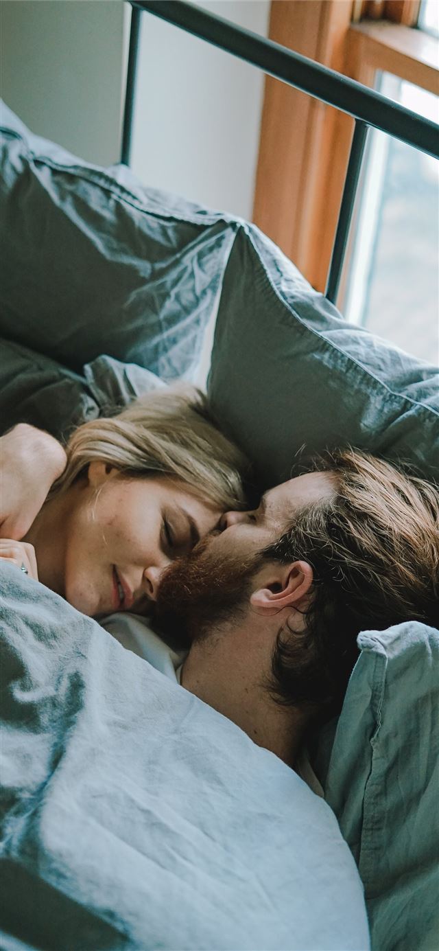 1125x2436 man kissing woman's forehead while lying on bed - united kingdom iPhone 11 Wallpaper