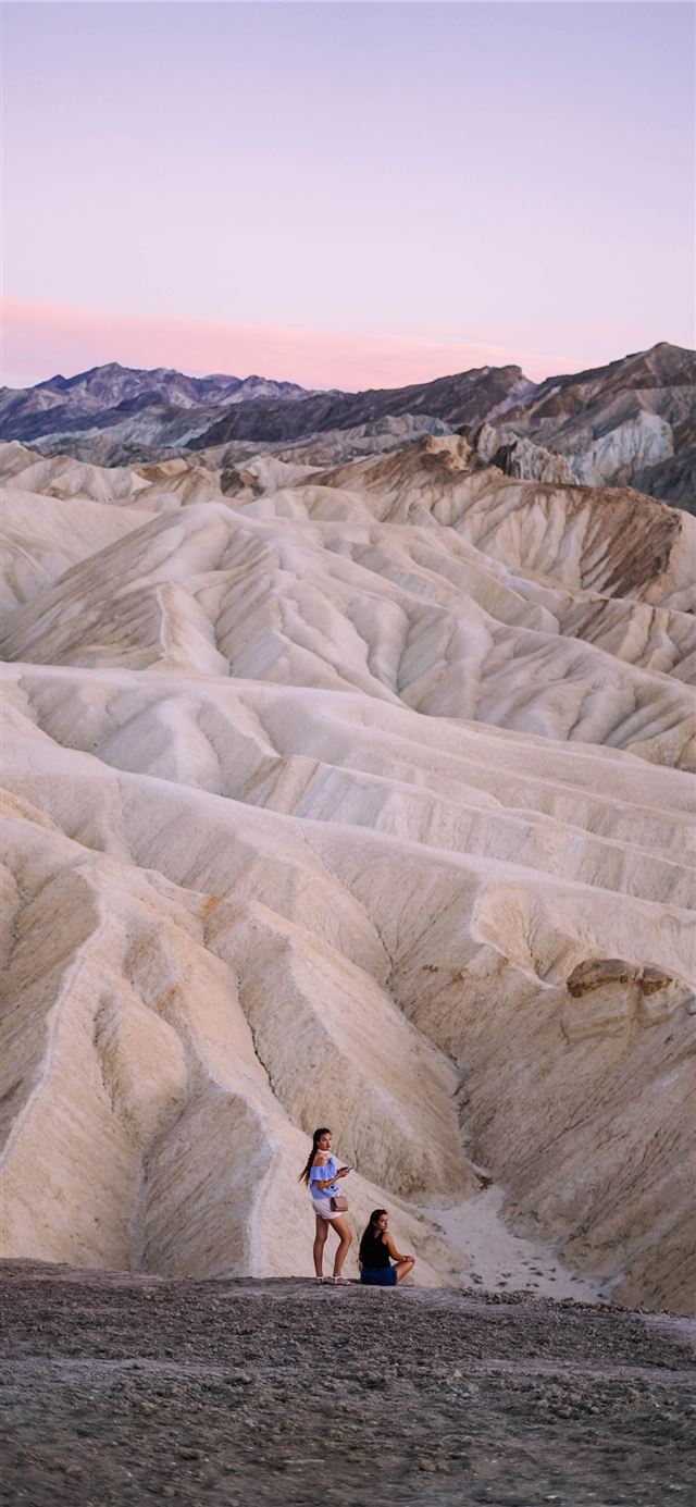 1125x2436 two people standing near sand dunes - death valley iPhone 11 Wallpaper