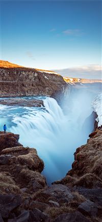 person standing on cliff near large waterfalls und... iPhone 11 wallpaper