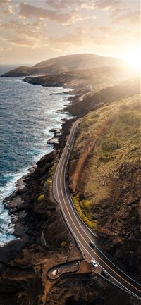 vehicles passing on road beside body of water duri... iPhone 11 wallpaper