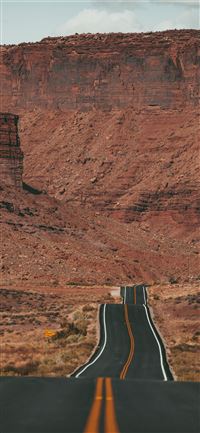 white car on road near brown rock formation during... iPhone 11 wallpaper