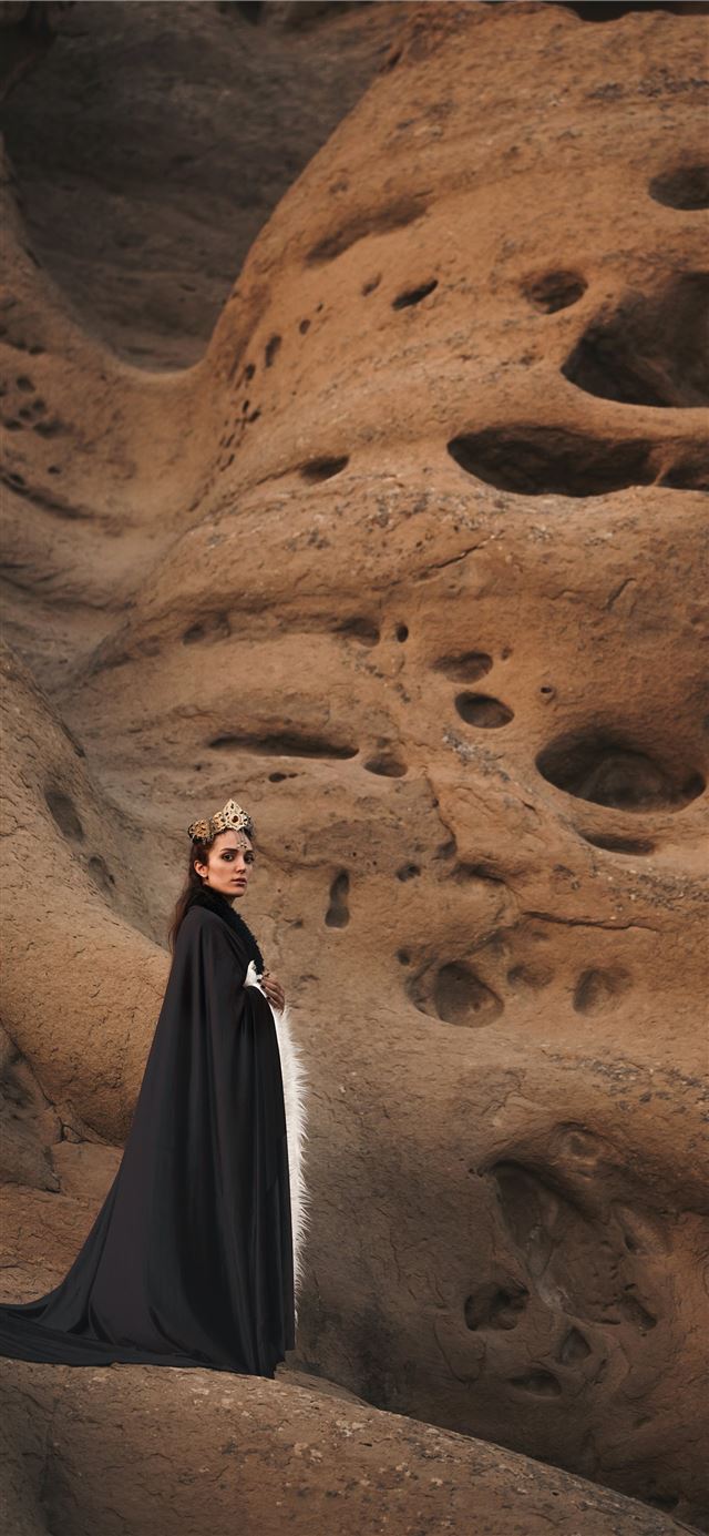 woman in black cape standing on brown mountain iPhone 12 wallpaper 