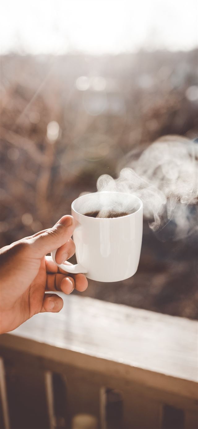 person holding white ceramic cup with hot coffee iPhone 12 wallpaper 