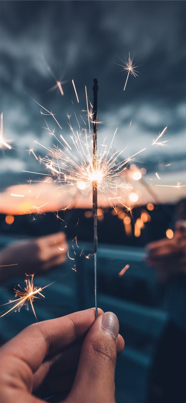photo of person holding lighted sparkler iPhone 12 wallpaper 