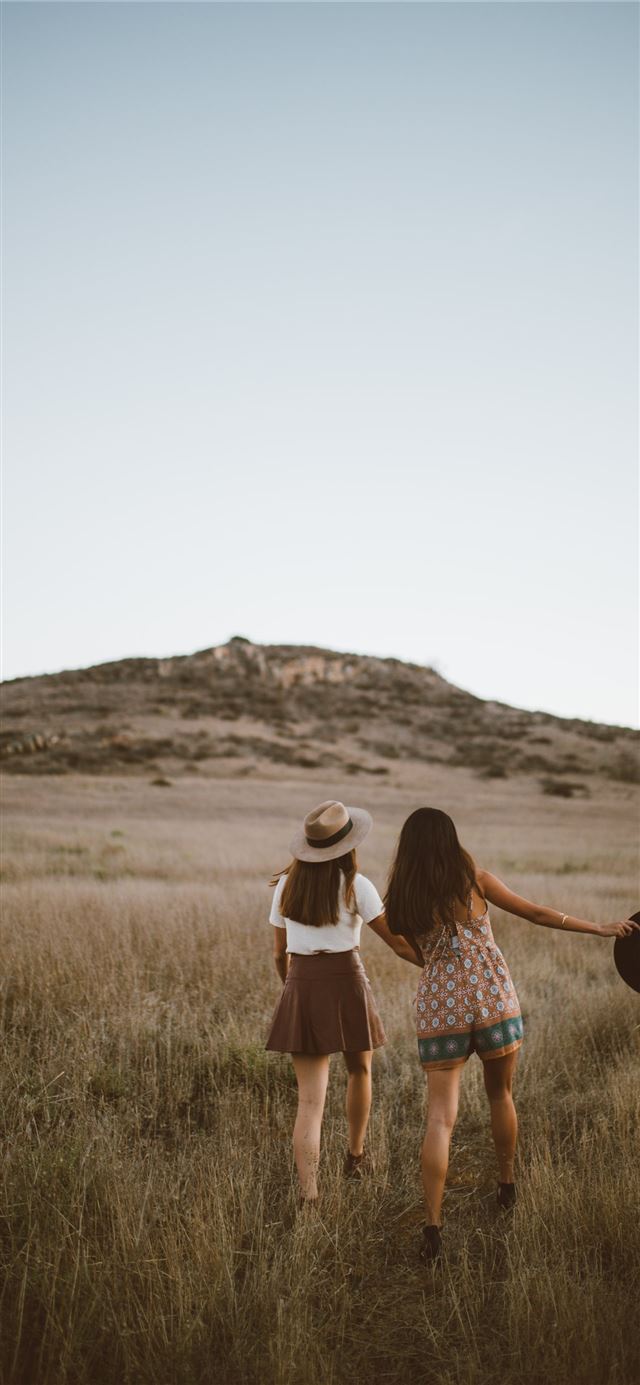 two women walking around near mountain at daytime iPhone 12 wallpaper 