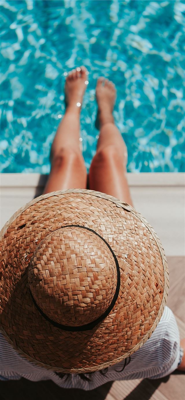 woman sitting on poolside setting both of her feet... iPhone 12 wallpaper 