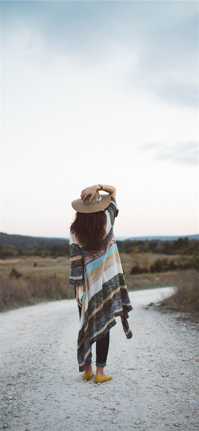 standing woman holding her hat at the middle of th... iPhone 12 wallpaper 