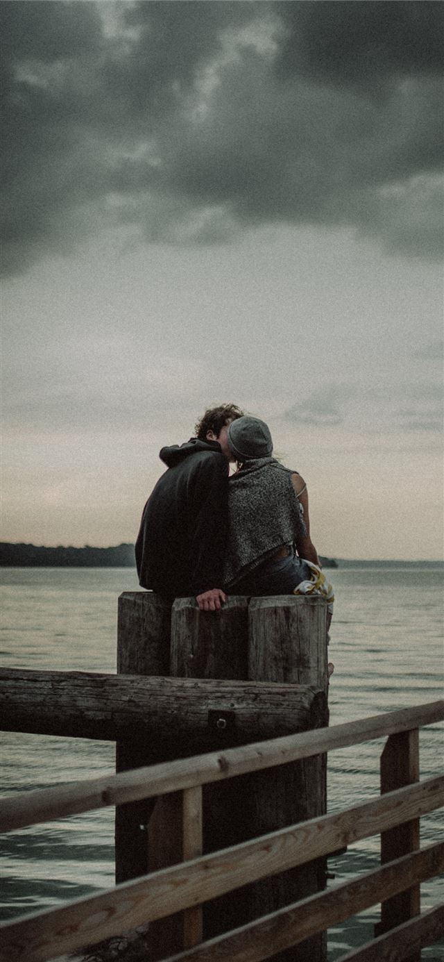 man and woman sitting and kissing on post near the... iPhone 12 wallpaper 