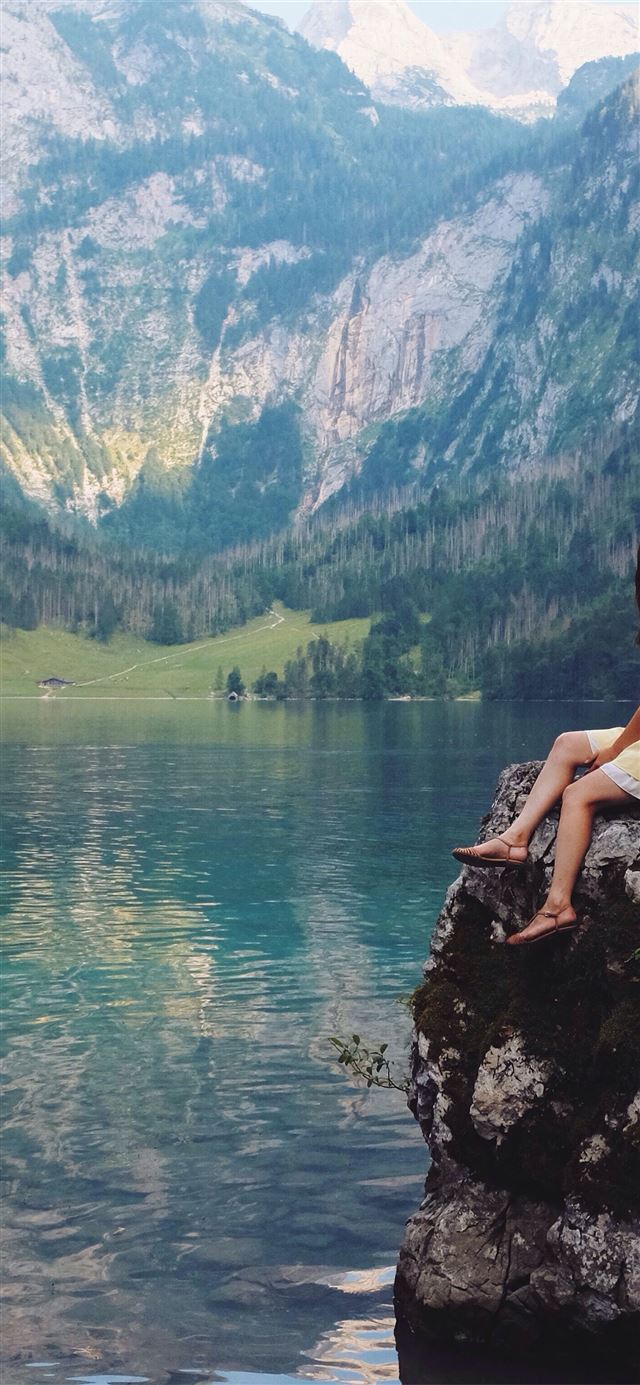 woman sitting on rock near lake iPhone 12 wallpaper 