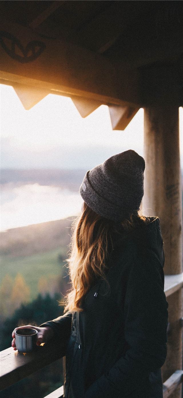 woman holding cup while looking outside iPhone 12 wallpaper 