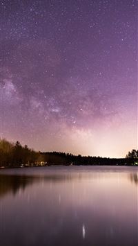 calm body of water overlooking trees under milky w... wallpaper