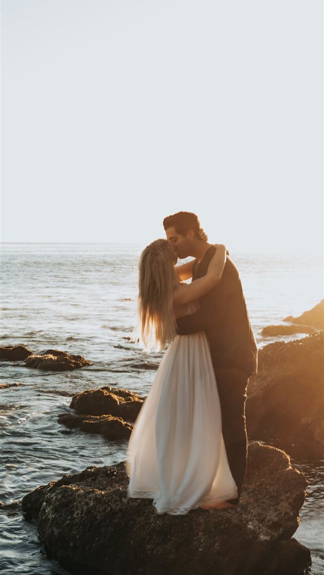 1284x2778 man and woman kissing on top of gray rock at beach - love iPhone Wallpaper