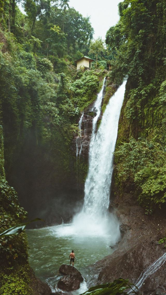 1284x2778 man standing on top of rock near waterfalls - indonesia iPhone Wallpaper