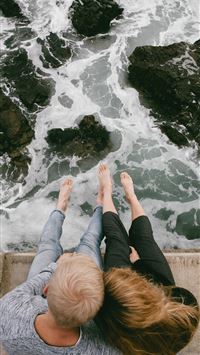 man and woman sitting on cliff near body of water wallpaper