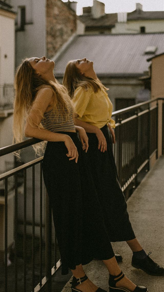 1284x2778 two women looking up white leaning on fence - poland iPhone Wallpaper