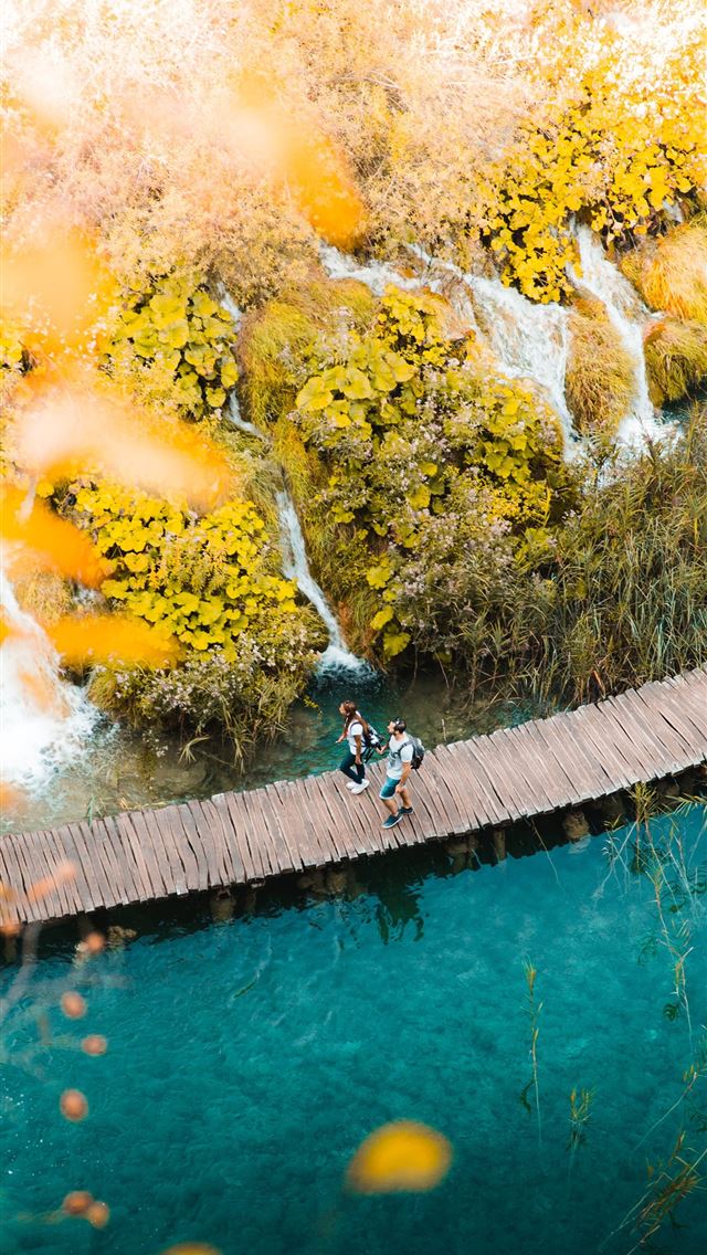 1290x2796 two person walking on boardwalk over body of water - bright iPhone Wallpaper