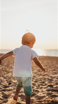 boy standing on sand near sea wallpaper