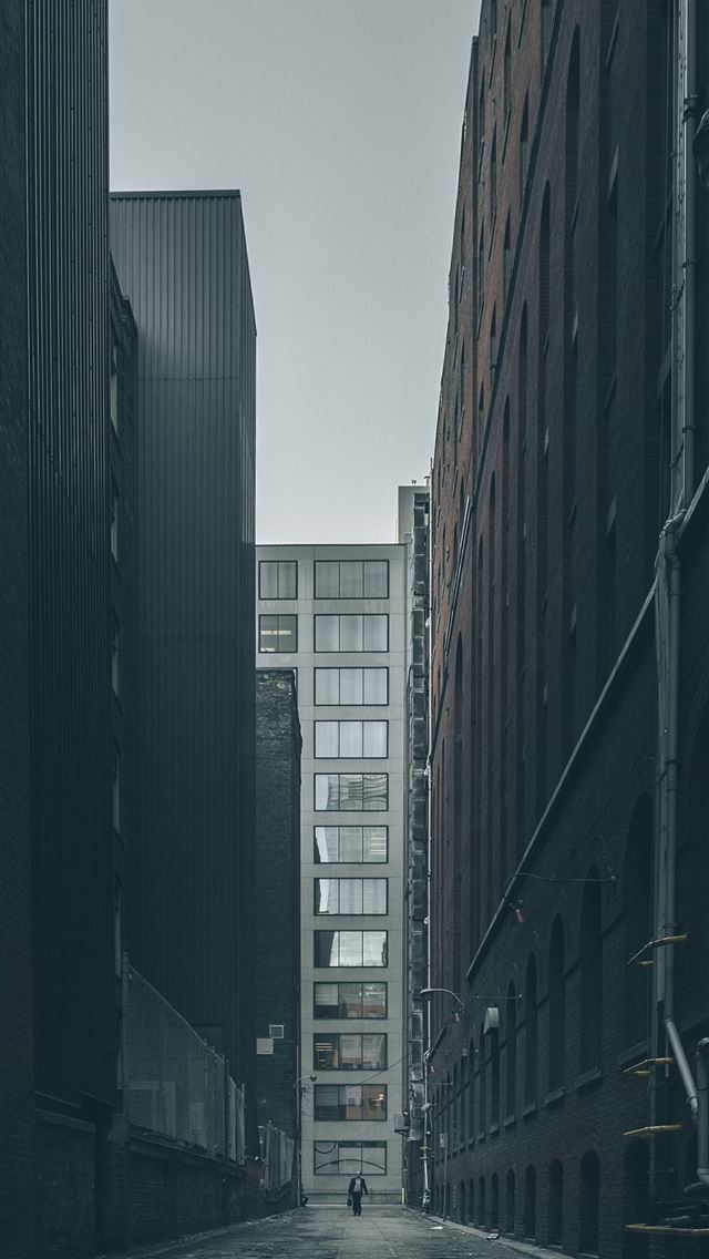 1290x2796 man walking in the middle of city buildings under ... - grey iPhone Wallpaper