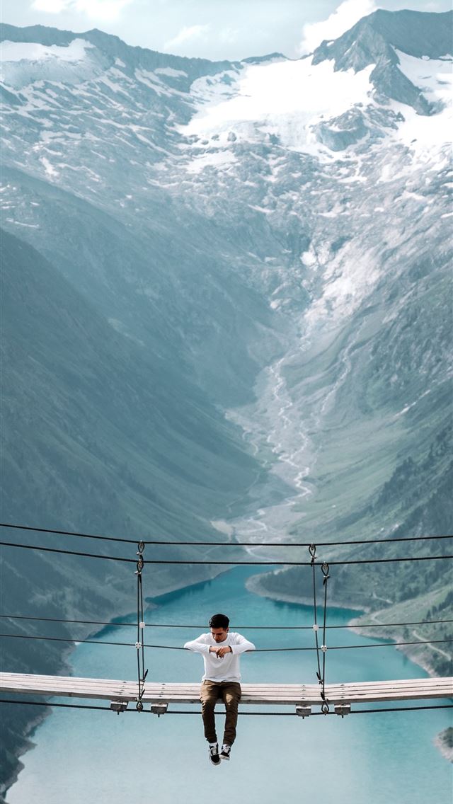 1290x2796 man sits on the hanging bridge between mountains - bridge iPhone Wallpaper