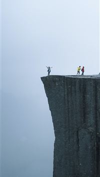 three persons standing near the edge of a cliff du... wallpaper