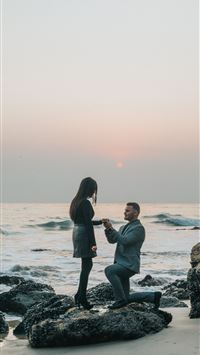 man kneeling in front of woman on rock at beach wallpaper