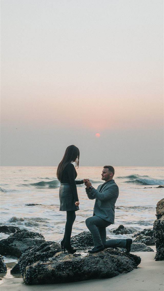 1290x2796 man kneeling in front of woman on rock at beach - love iPhone Wallpaper