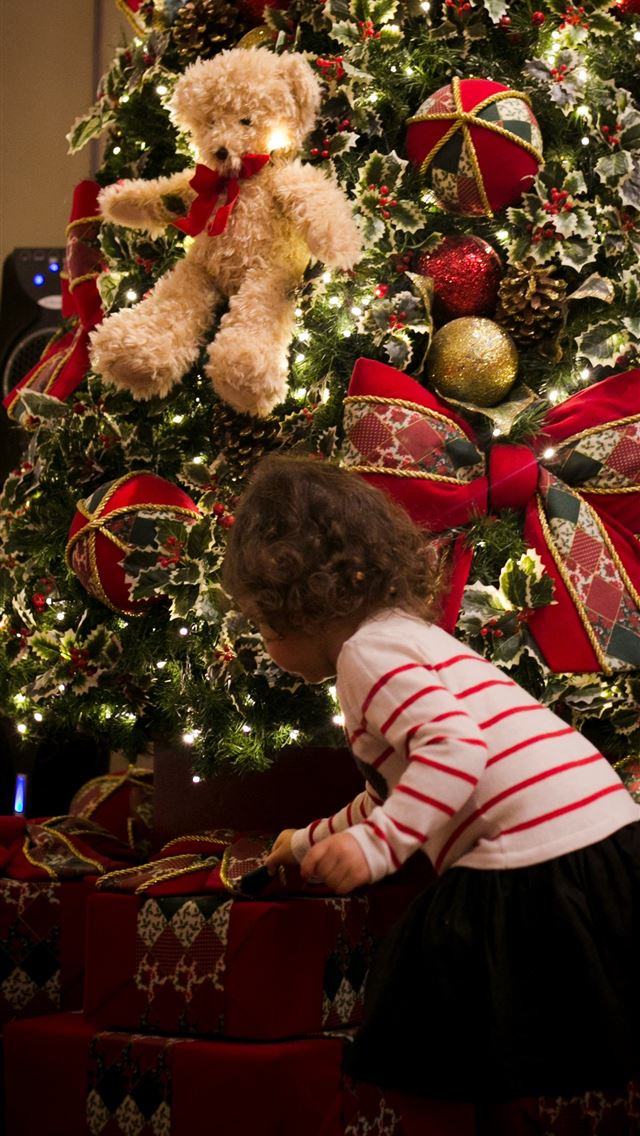 1290x2796 girl picking gift in front of pre lit tree - christmas tree iPhone Wallpaper