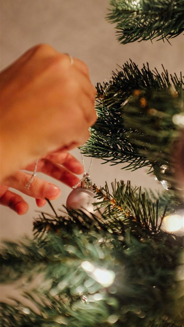 1290x2796 person putting bauble on Christmas tree -  iphone 15 Wallpaper