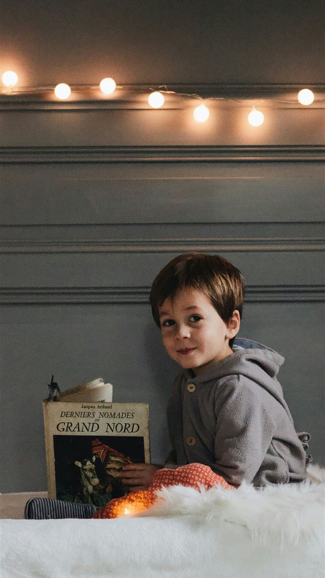1290x2796 boy holding a book while sitting on top of bed - baby iPhone Wallpaper