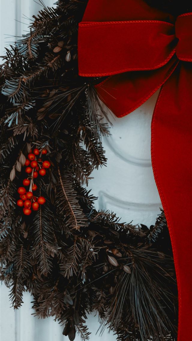 1290x2796 a wreath with a red bow hanging on a door - holidays iPhone Wallpaper