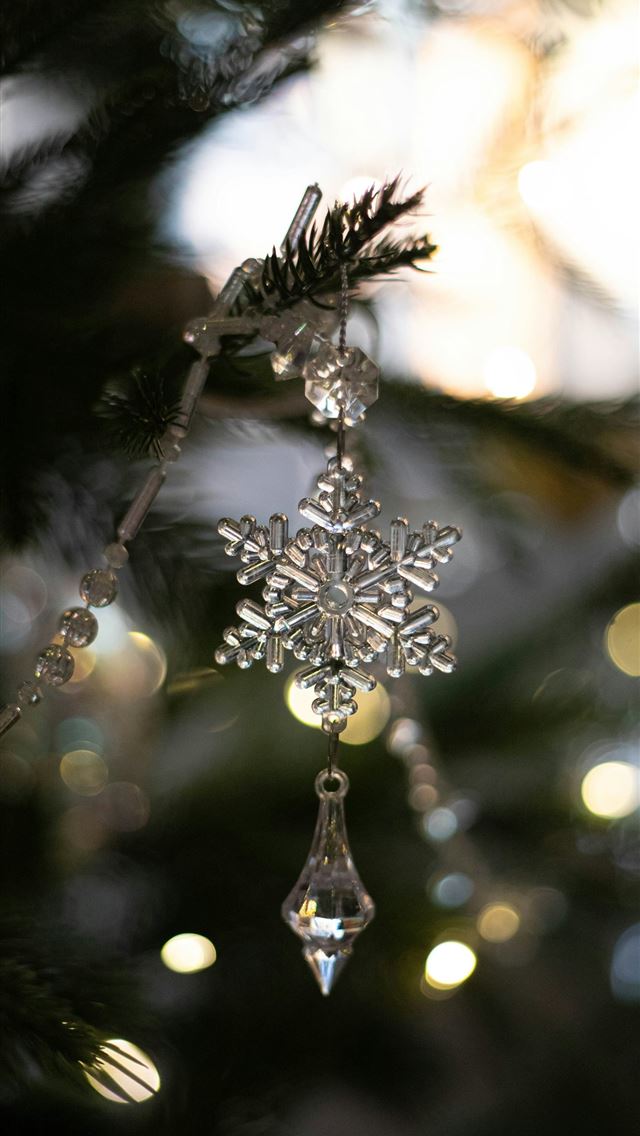 1290x2796 a snowflake ornament hanging from a christmas tree - tree iPhone Wallpaper