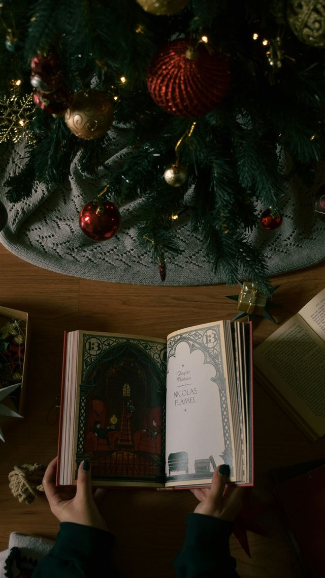 1290x2796 A person reading a book in front of a christmas tr... - christmas iPhone Wallpaper