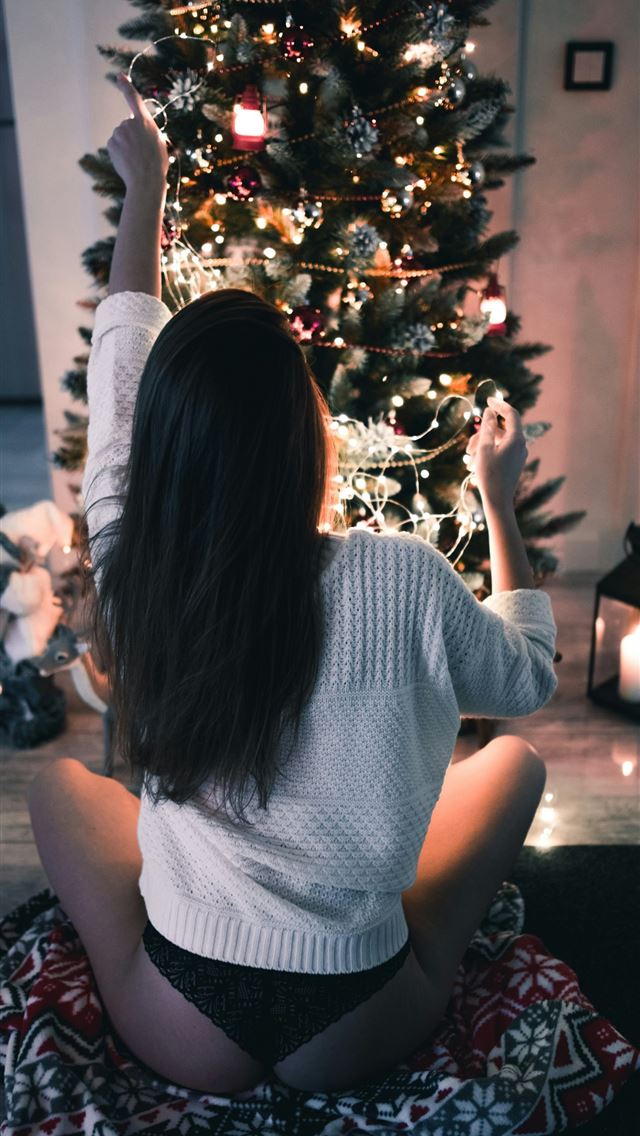1290x2796 woman sits on red textile infront of Christmas tre... -  iPhone Wallpaper