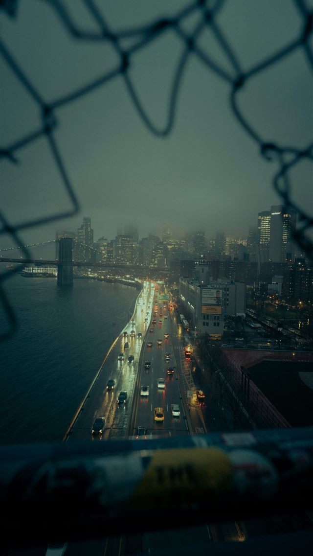 1290x2796 A view of a city from behind a chain link fence -  iPhone Wallpaper