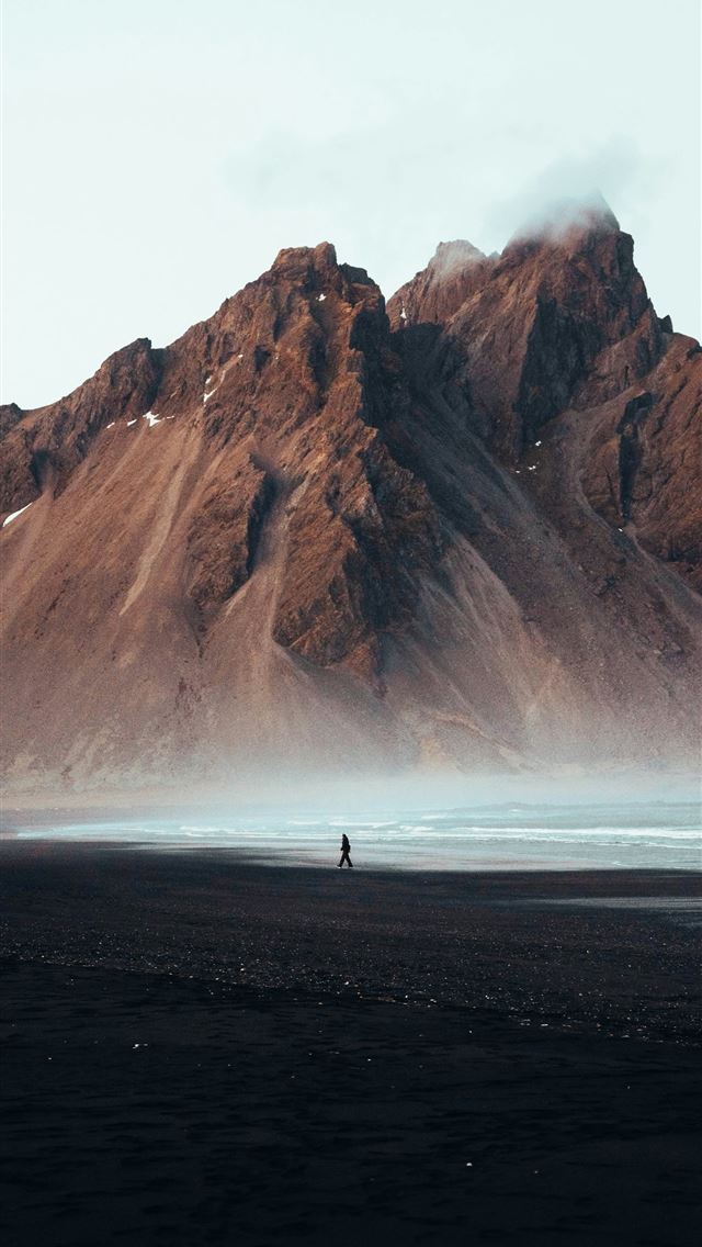 1290x2796 A person stands on a beach before a mountain  -  iPhone Wallpaper
