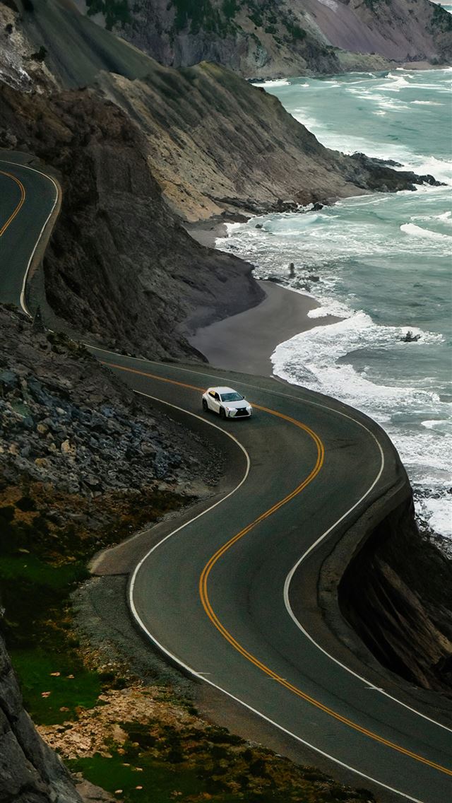 1290x2796 A car driving down a road next to the ocean -  iPhone Wallpaper