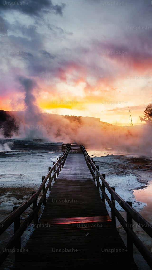 1290x2796 a boardwalk leading to a steaming geyser at sunset -  iPhone Wallpaper