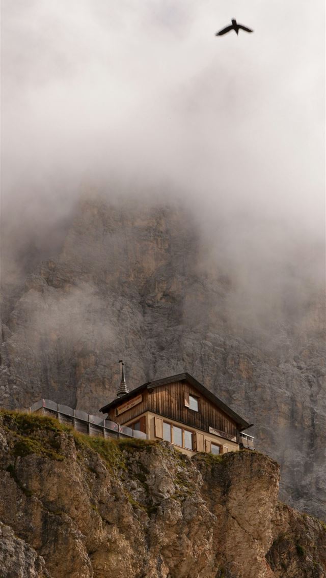 1290x2796 a bird flying over a house on a cliff -  iPhone Wallpaper