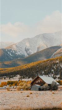 a small cabin in the middle of a field with mounta... wallpaper