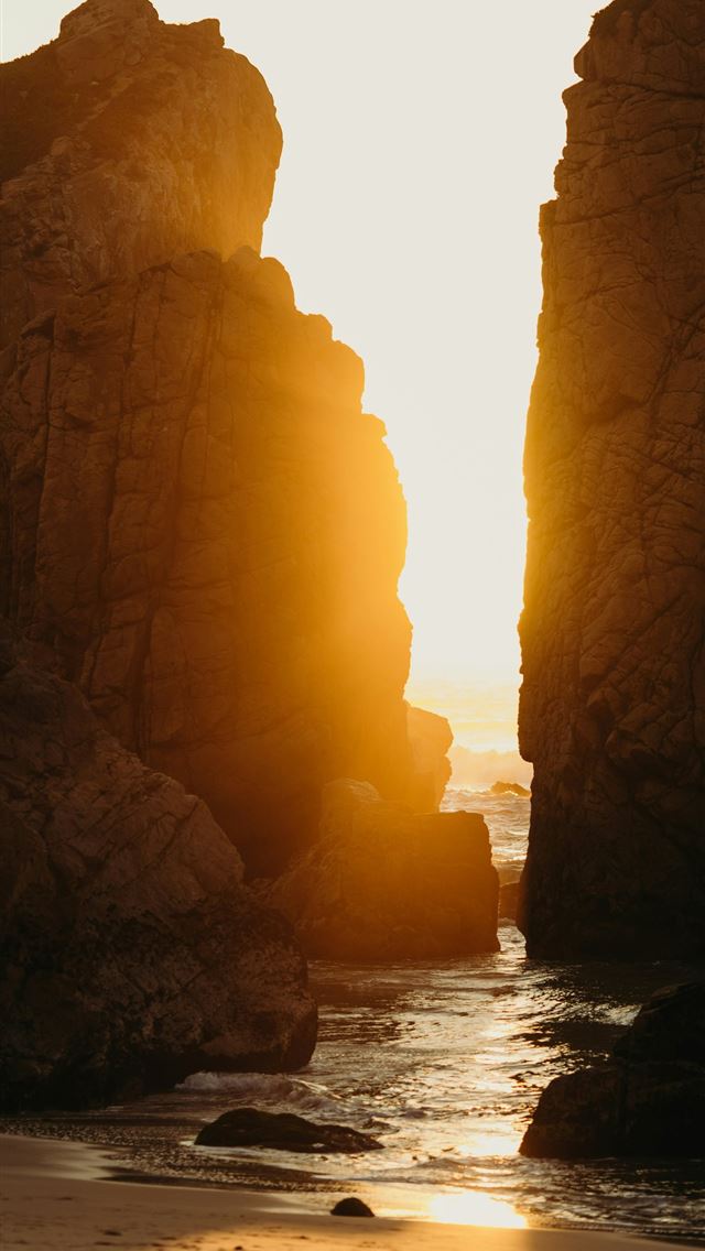 1290x2796 the sun is setting on the beach by the rocks - sea iPhone Wallpaper