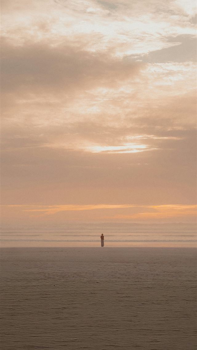 1290x2796 A lone figure stands on a vast beach at sunset  -  iPhone Wallpaper