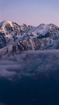 Snow capped mountains emerge from misty clouds at ... wallpaper