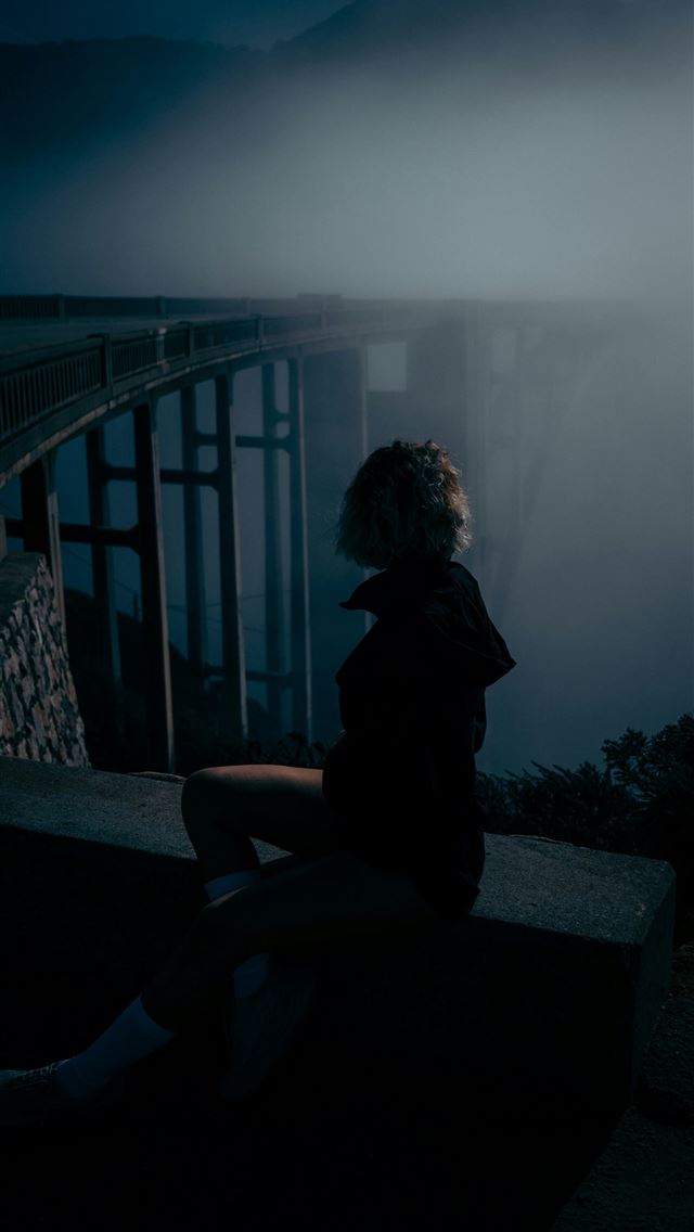 1290x2796 Woman sitting on ledge near foggy bridge at night -  iPhone Wallpaper