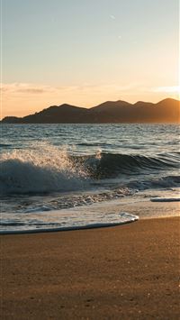 Gentle waves wash onto a sandy beach at sunset  wallpaper