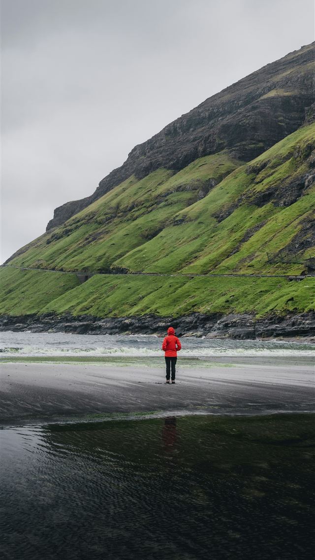 1290x2796 A person in a red jacket standing on a beach - sea iPhone Wallpaper
