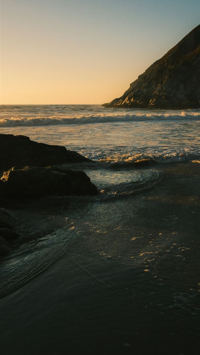 1290x2796 Waves gently lap against dark rocks at sunset - sunset iPhone Wallpaper